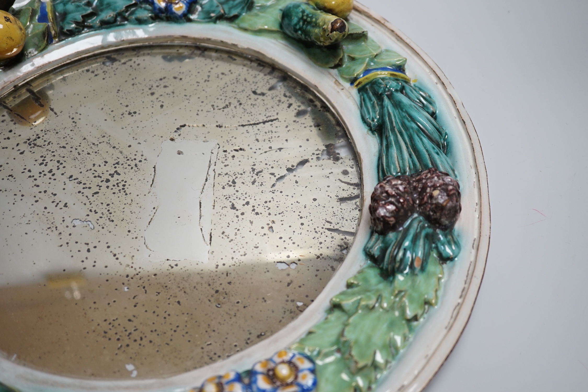 A circular earthenware mirror, possibly by Della Robbia Pottery of Liverpool, decorated with foliage and fruit, 37cm